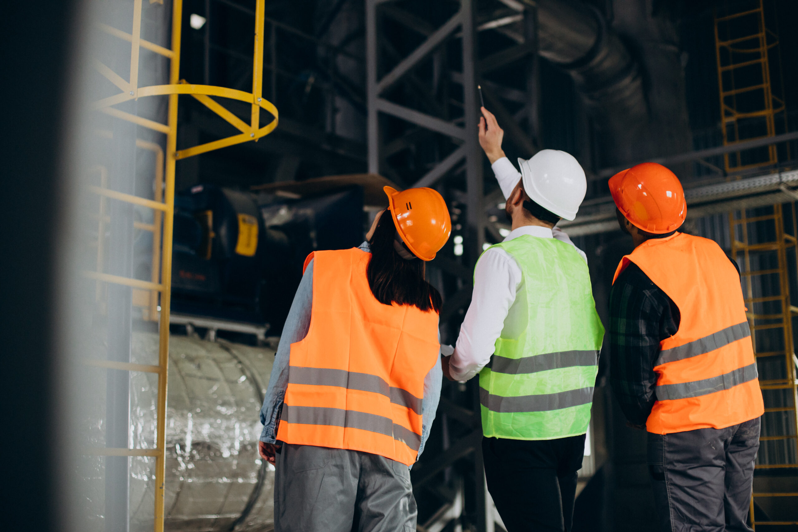 Three factory workers in safety hats discussing manufacture plan Three factory workers in safety hats discussing manufacture plan